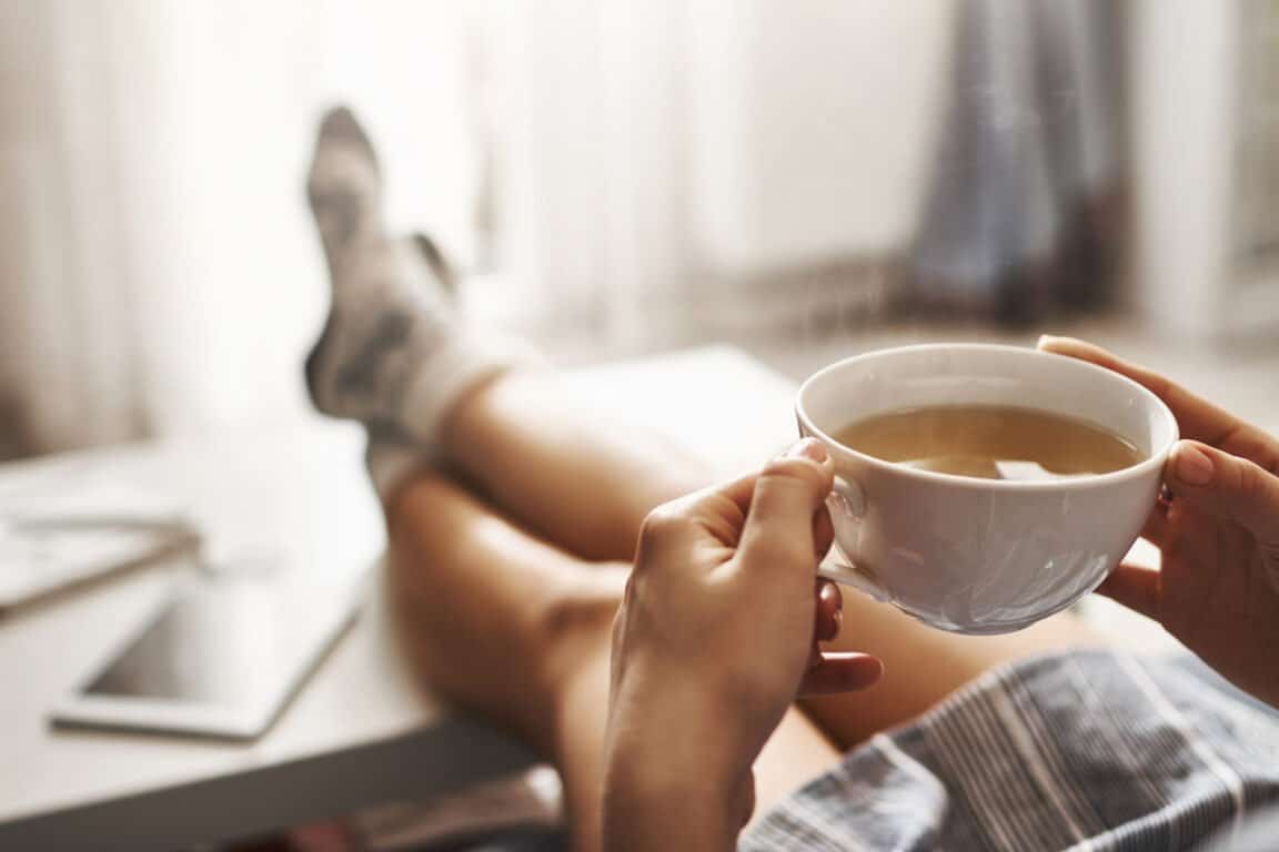 Journée Mondiale de l'habitat - personne assise les jambes allongées sur la table basse et tenant une tasse de thé